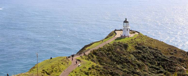 Groene heuvels met een witte vuurtoren tegen de blauwe zee bij Cape Reinga in Nieuw-Zeeland
