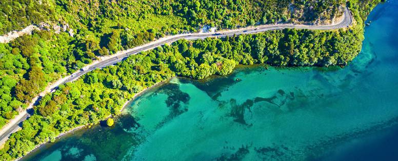 Lake Taupo vanaf boven met de groene heuvels en lichtblauwe oceaan en een autoweg.